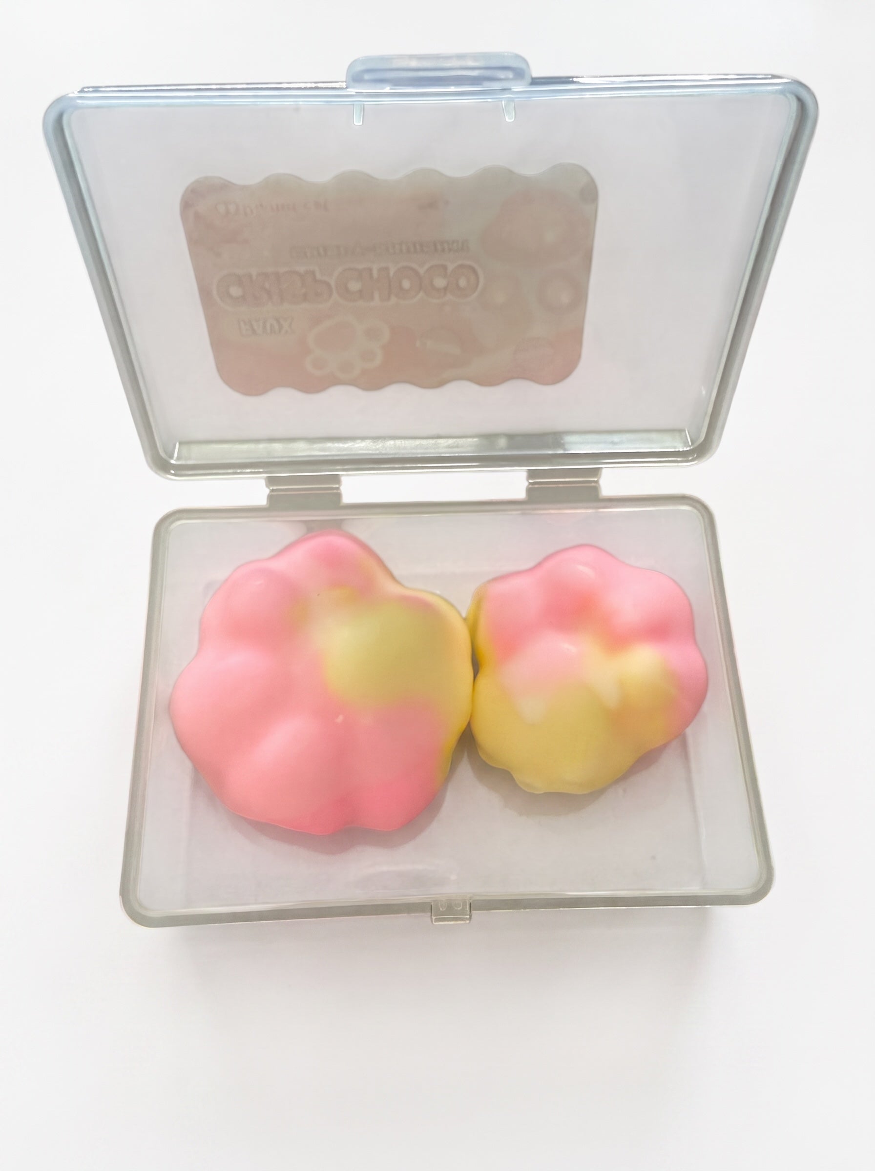 Le Sage May faux chocolate paw-shaped squishy toys in pink and yellow, stored in a clear plastic display case.